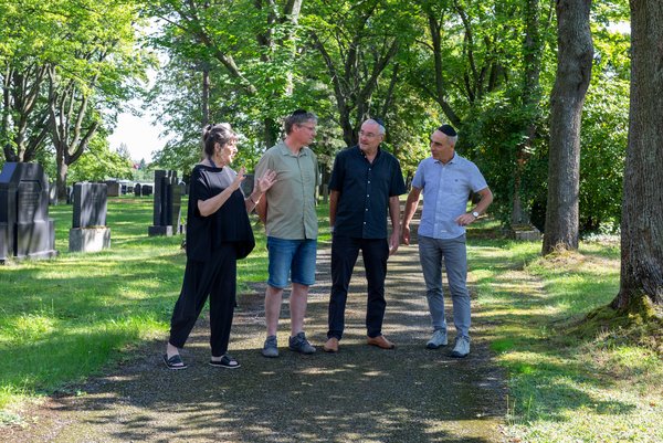 Vier Personen auf einem parkähnlichen jüdischen Friedhof