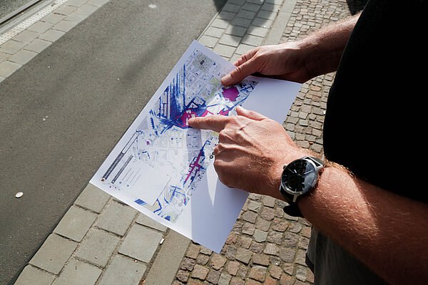 Starkregengefahrenkarte Tilo Sahlbach steht am Friedrich-List-Platz und hält eine ausgedruckte Starkregengefahrenkarte in der Hand.